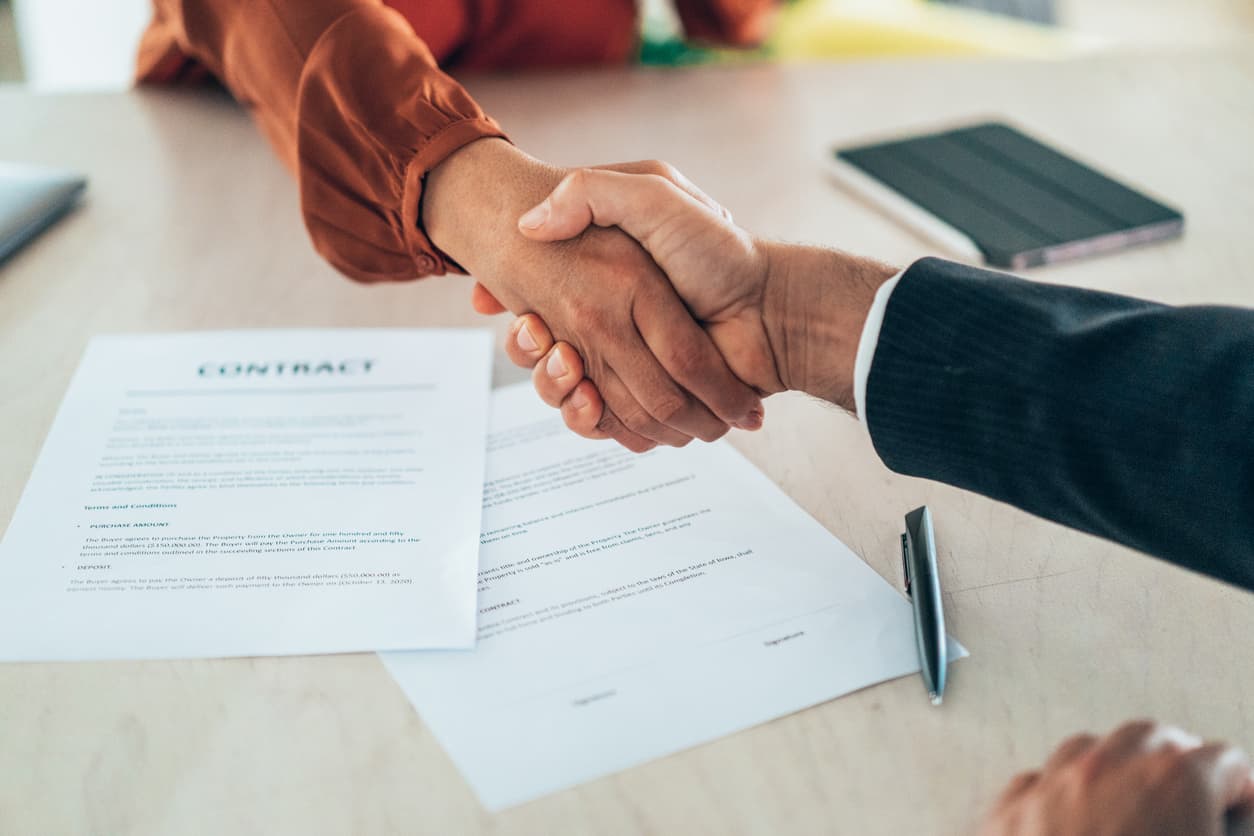 Two people shake hands over a signed contract with tablet nearby.